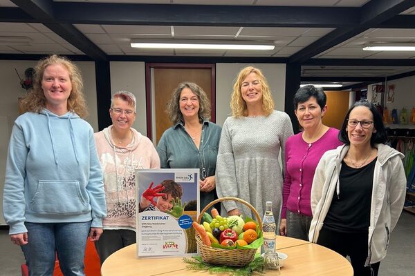 Sechs Frauen stehen um einen Tisch auf dem sich in der Mitte ein Obstkorb und das aufgestellte Zertifikat befindet